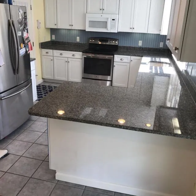 Kitchen with a grey tile floor, dark granite counters and a blue beadboard backsplash, installed on Cape Cod